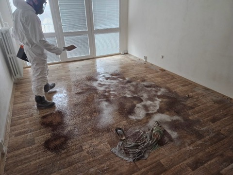 Pracovník v ochranném obleku provádějící dezinfekční zásah v bytě po úmrtí.