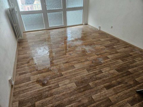 Mokrá, vyčištěná podlaha v prázdném bytě po odborném čištění v rámci dezinfekce po úmrtí.