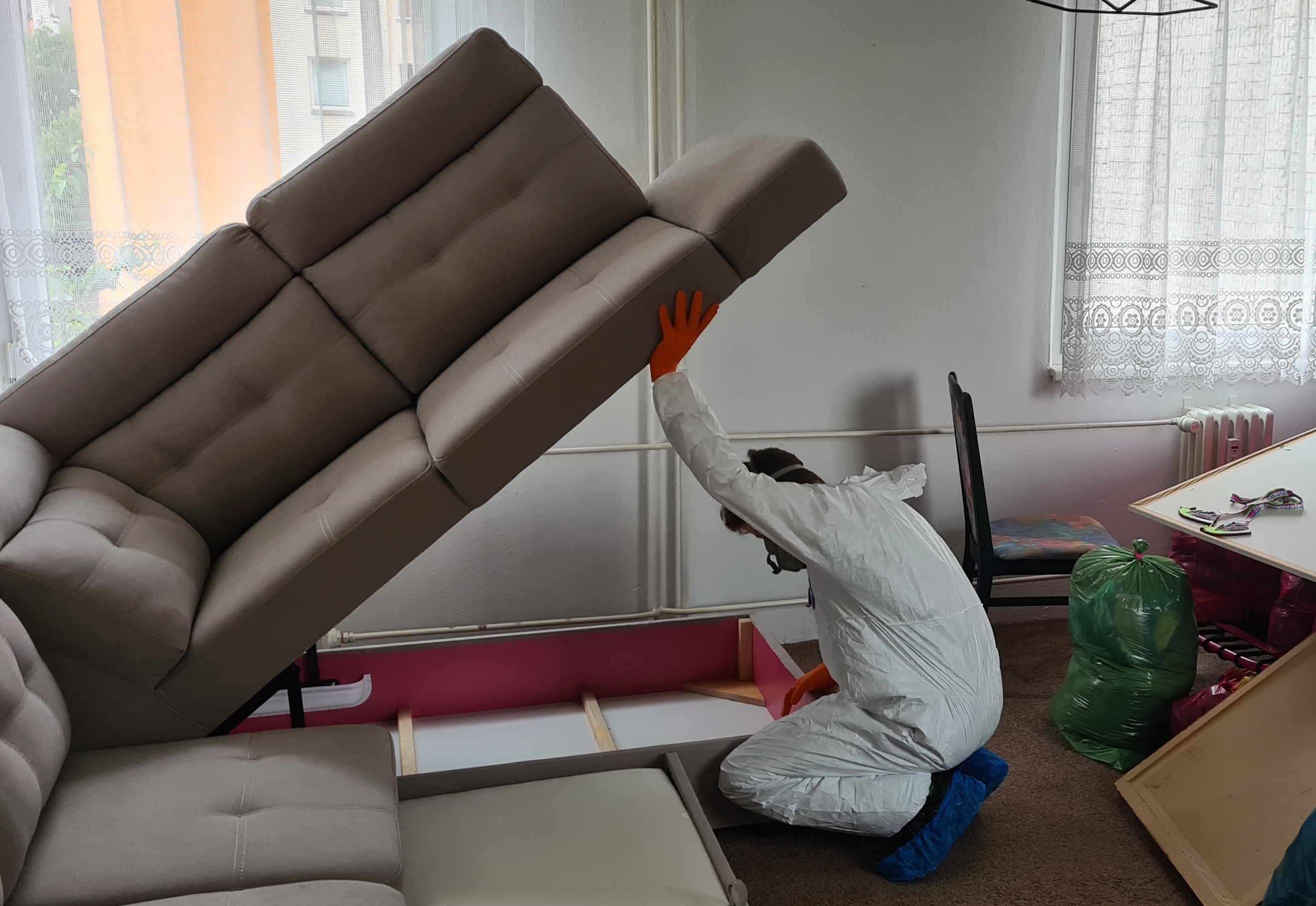 Pracovník v ochranném obleku kontroluje čalouněnou sedačku během zásahu proti štěnicím.